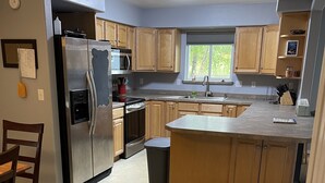 A kitchen with wooden cabinets, a stainless steel refrigerator, a microwave, a sink, and a window.