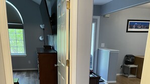 A hallway with a wooden floor, a white door, a wooden dresser, and a refrigerator.