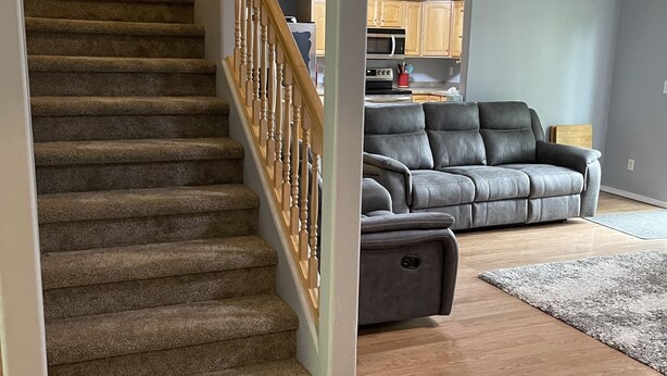 A staircase with carpeted steps and wooden railings leading to a living area with a gray leather sofa, a wooden coffee table, and a rug on a wooden floor.