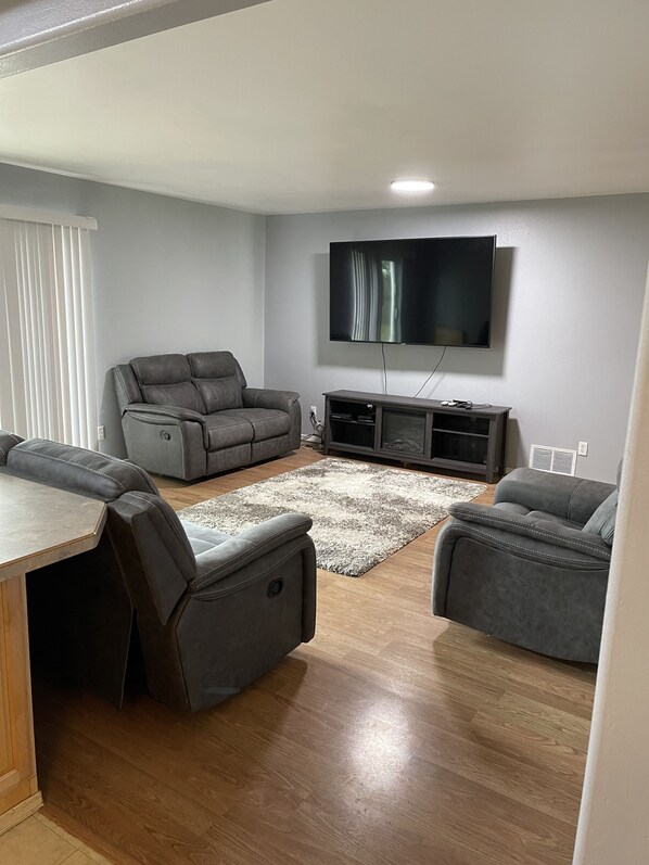 A modern living room with a grey sofa, a TV mounted on the wall, and a wooden floor.