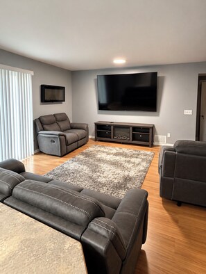 A modern living room with a large flat-screen TV, leather sofas, and a wooden floor. - Multi-Family House - Sleeps 16 (Anchorage)