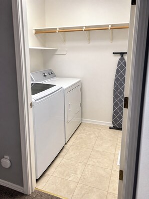 A laundry room with a washing machine, dryer, and ironing board. - Multi-Family House - Sleeps 16 (Anchorage)