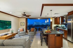 A modern kitchen with a central island, a dining area with a view of the cityscape, and a living room with a sofa and a coffee table.