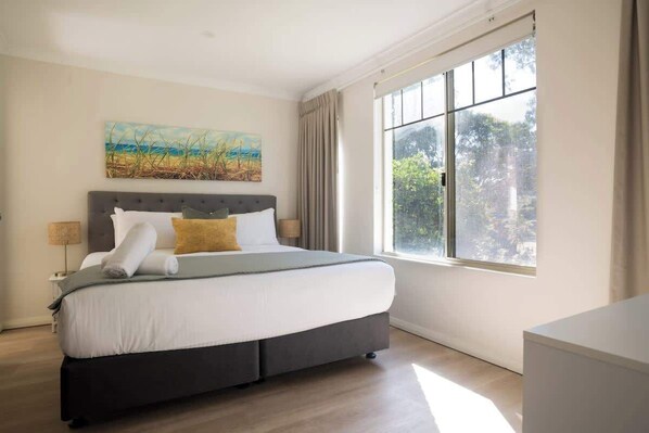 A bedroom with a large bed, a painting on the wall, and a window with curtains.