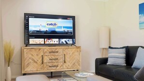 Un soggiorno moderno con una TV a schermo piatto montata su un mobile in legno, un divano in pelle nera e un tavolino da caffè in vetro.