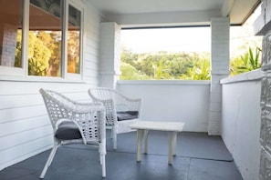 A white wicker chair and table on a balcony with a view of trees. - Higgins Hideaway—Central Cottage with Garden Oasis (Margaret River)