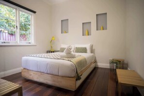 A bedroom with a wooden bed, a window, a bedside table, and a lamp.