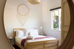 Une chambre avec un lit en bois, du linge de lit blanc, un attrape-rêves, des lampes de chevet et une fenêtre donnant sur un beau paysage.