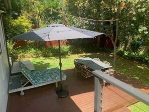 A deck with a table and chairs, a lounge chair, and a large umbrella providing shade.