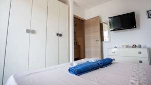 Un dormitorio con cama, televisor montado en la pared, armario y cómoda.