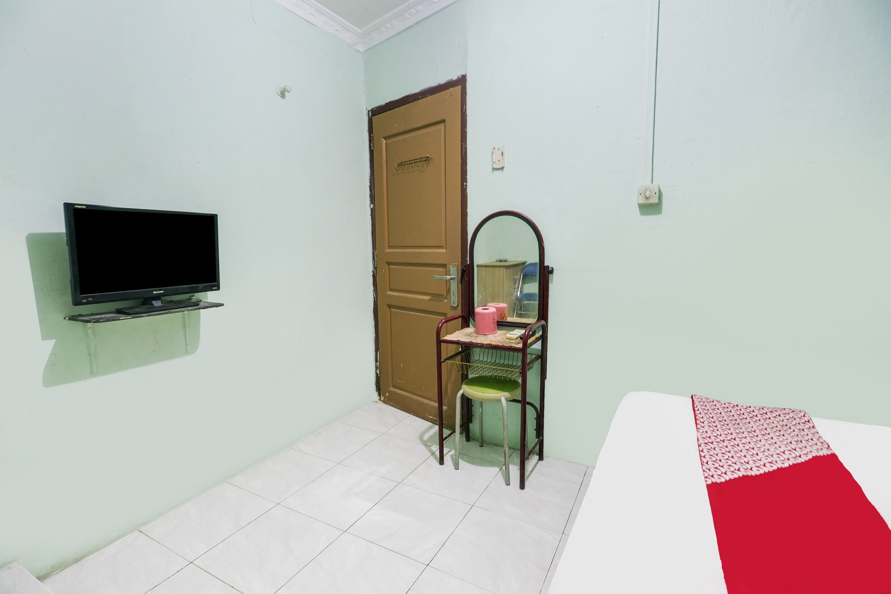 A room with a bed, a television mounted on the wall, a door, and a chair with a mirror.