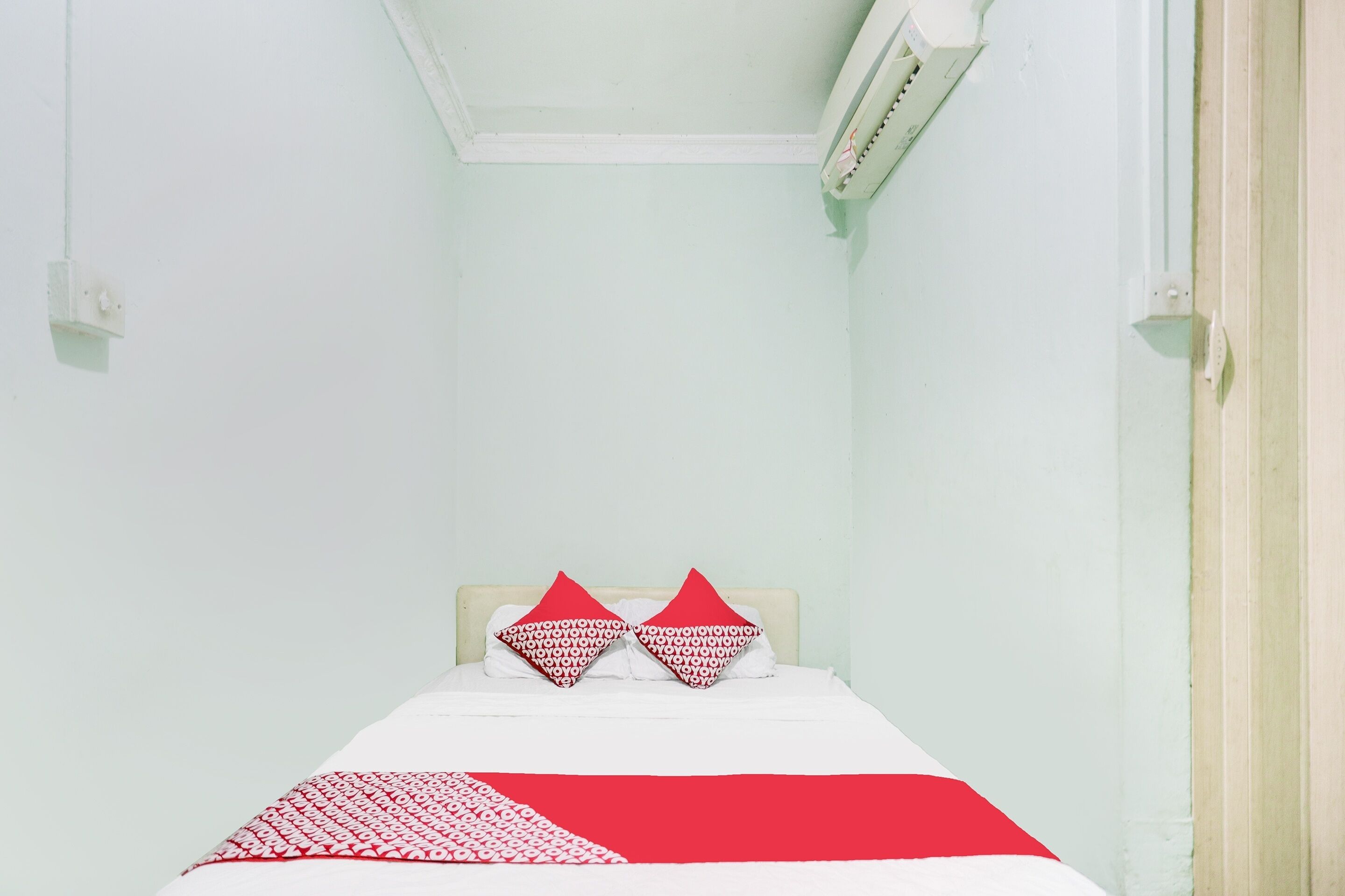 A narrow room with a bed, two pillows, and a red and white bedspread.