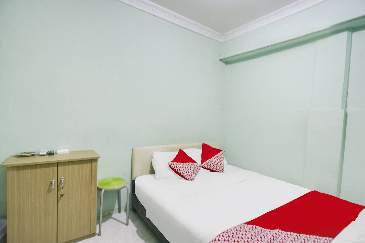 A room with a bed, a wooden cabinet, and a small stool.