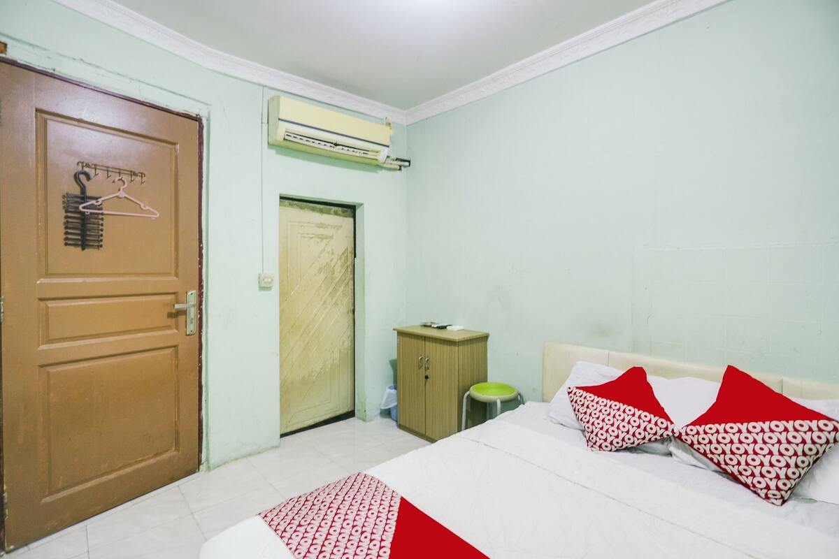 A bedroom with a bed, pillows, a wardrobe, a door, and an air conditioning unit.
