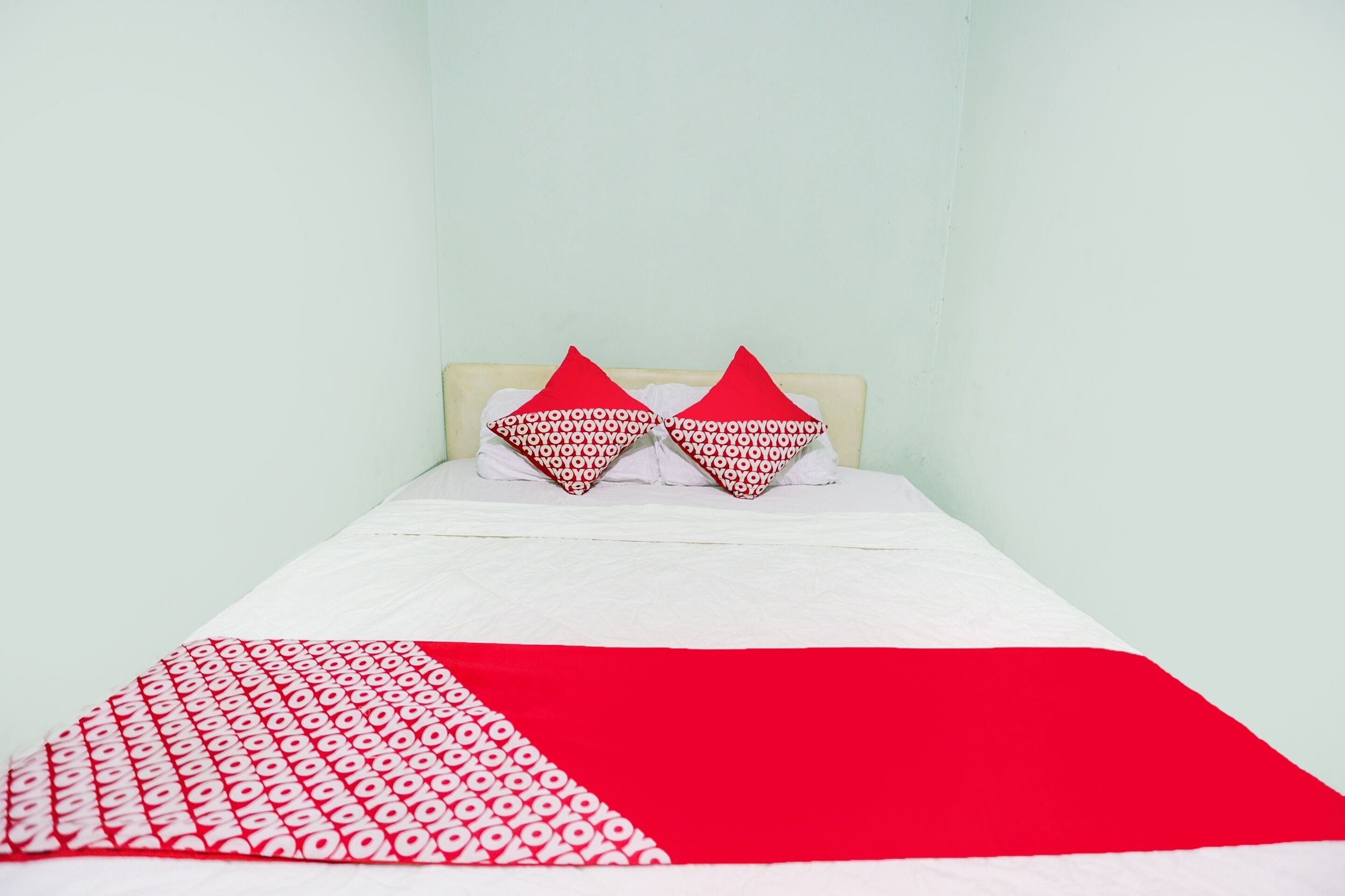 A bed with a white and red bedspread, two red pillows with white patterns, and a plain light-colored wall.