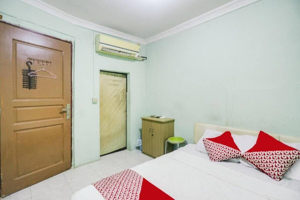 A bedroom with a bed, pillows, a wardrobe, a door, and an air conditioning unit.