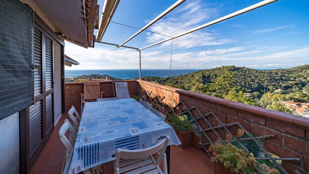 A terrace with a table and chairs, overlooking a scenic landscape with hills and a view of the sea. - Cala Azzurra in Fetovaia (Campo nell'Elba)
