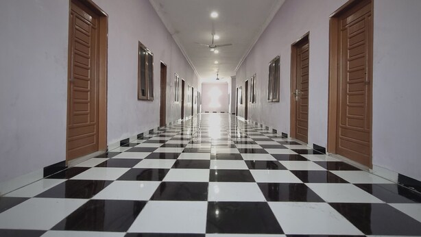 A long hallway with checkered black and white flooring, wooden doors on both sides, and a ceiling fan. - EXPRESS O 91979 Penginapan Tondong Ta (Medan)