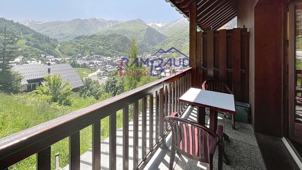 A balcony with a table and chairs overlooking a mountainous landscape with a village below. - Apartment 2 rooms 4 beds -Swimming pool - Footpath (VALLOIRE)