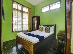 A room with a bed, a wooden headboard, a window with curtains, and a chair. - Hotel O Desa Wisata Selamanik Ciamis (Bangunharja)