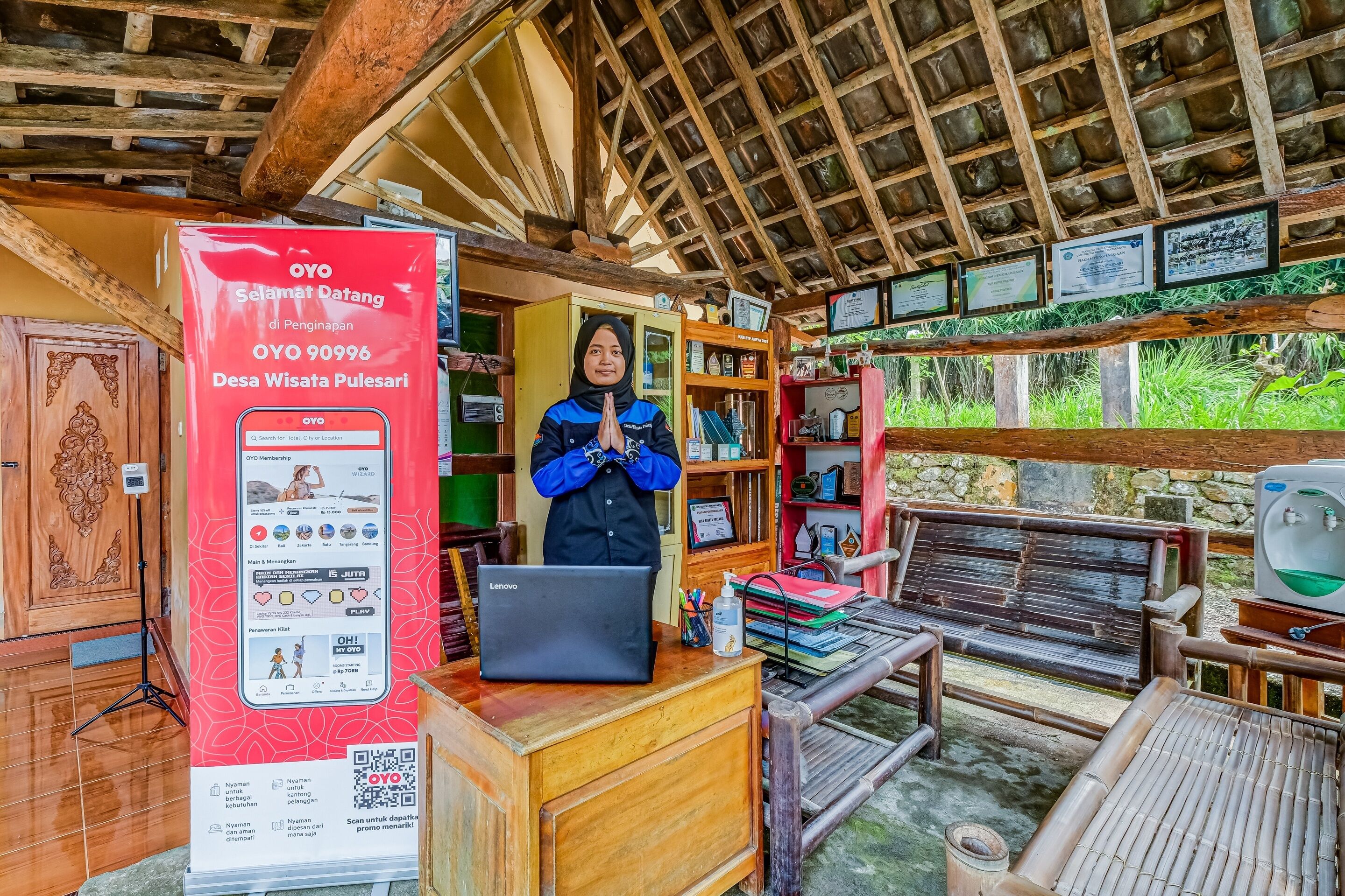 Eine traditionelle Holzhütte mit einem Reetdach, einem Empfangstisch mit einem Lenovo Laptop und einem Schild für OYO Selamat Datang.