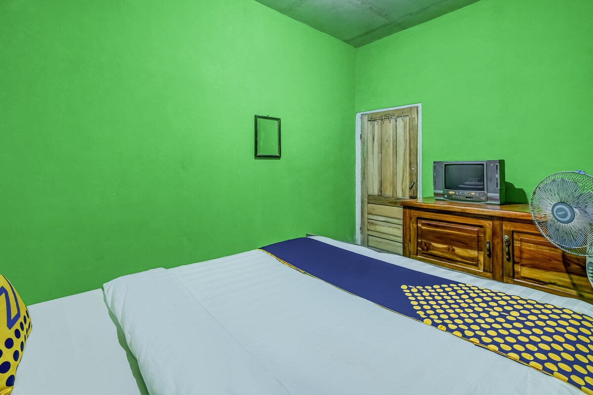 A room with a bed, a wooden dresser, a television, and a fan.