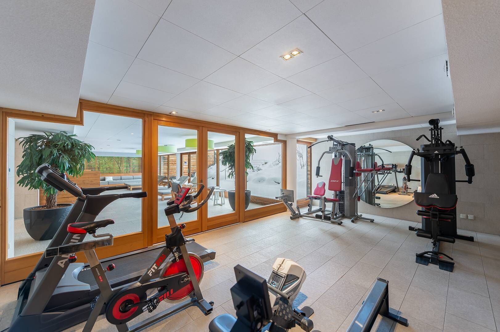 Un gimnasio amplio con máquinas de cardio, equipo de pesas y grandes ventanales con vistas al exterior.