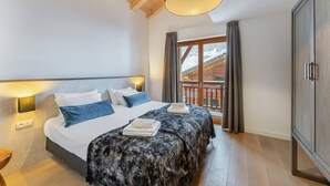 A bedroom with a large bed, a wooden ceiling, a window with curtains, and a view of a snowy landscape. - MONT BLANC - A08 - apartment for 8 people with 3 bedrooms (LA CHAPELLE D ABONDANCE)