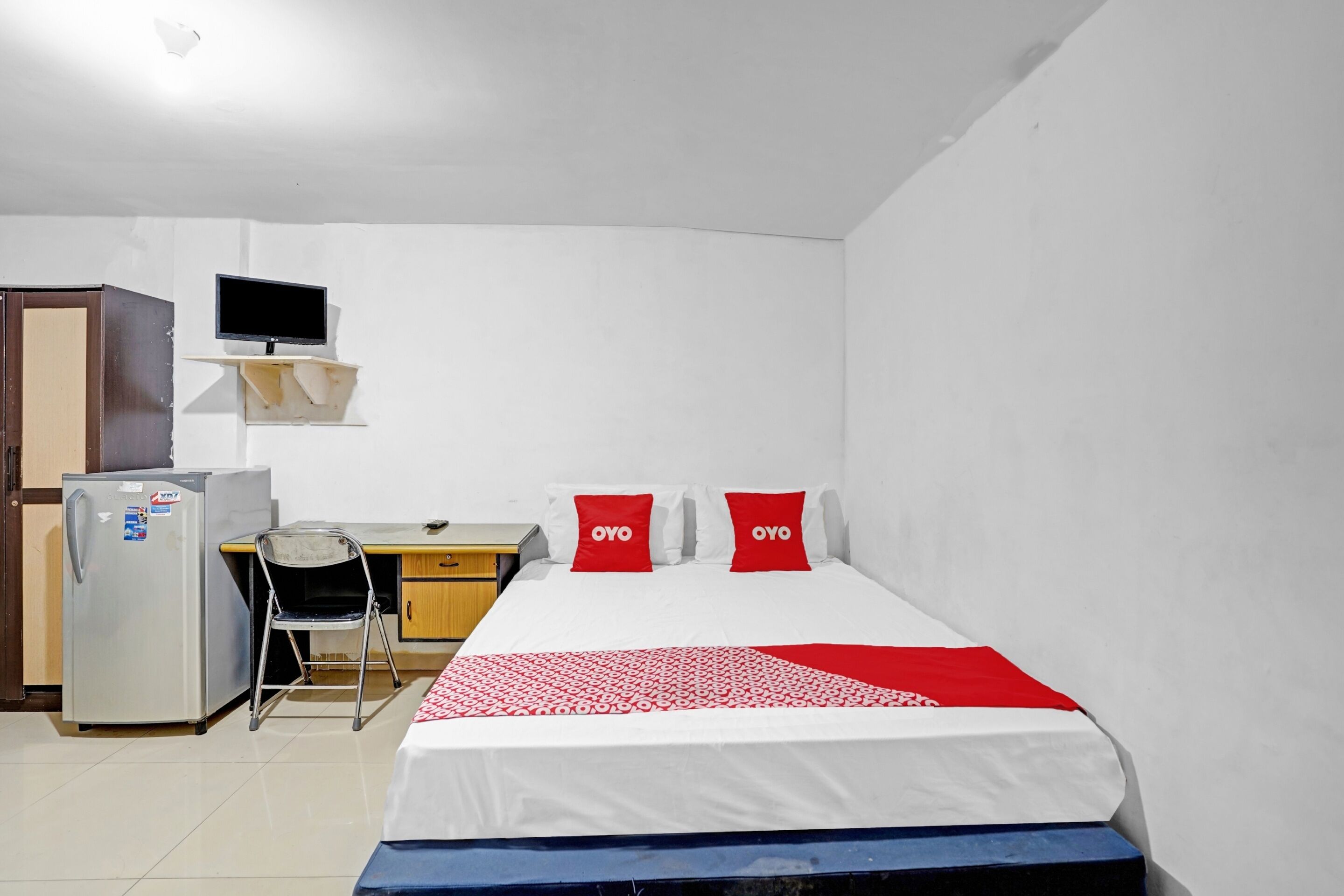 A small, clean room with a bed, a desk, a chair, a refrigerator, and a TV.