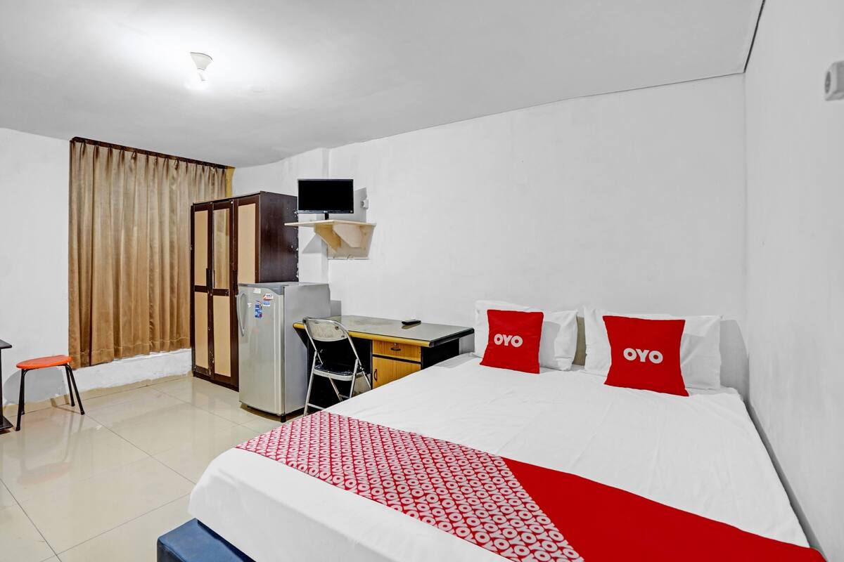 Een hotelkamer met een bed, bureau, stoel, koelkast en televisie.
