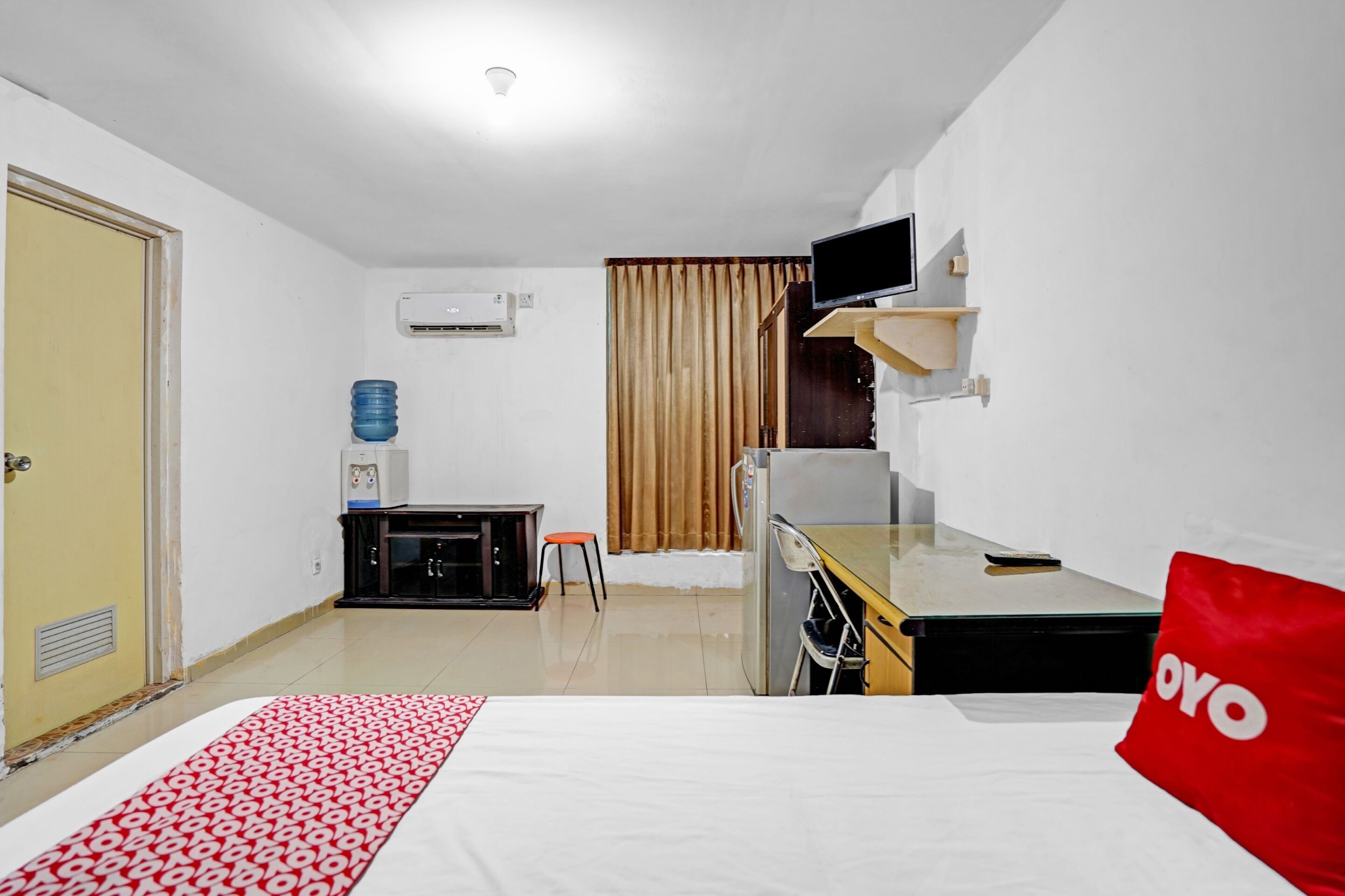 A hotel room with a bed, a desk, a chair, a TV, and a minibar.