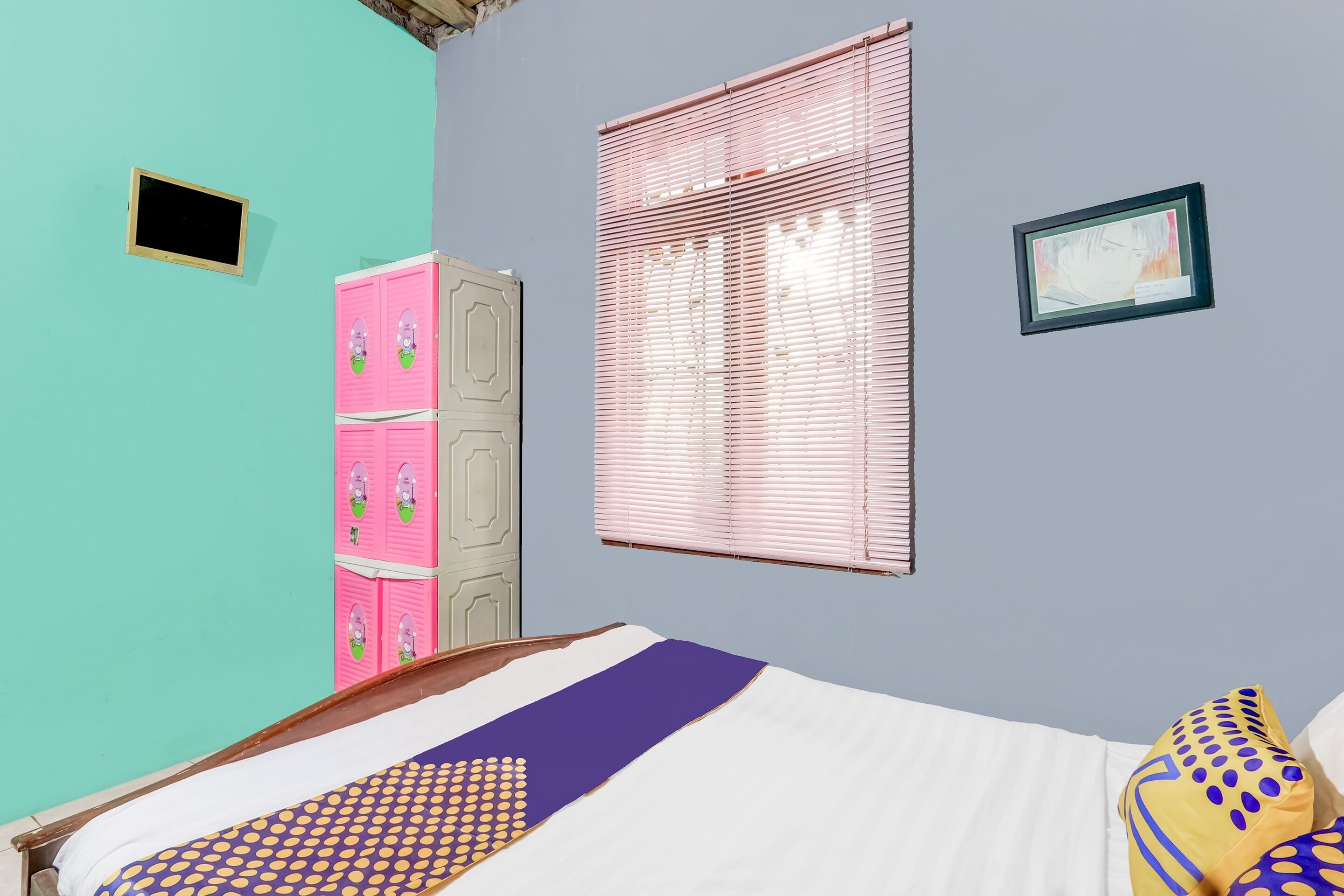 Un dormitorio con cama, un armario rosa, una ventana con persianas y un pequeño marco de fotos en la pared.