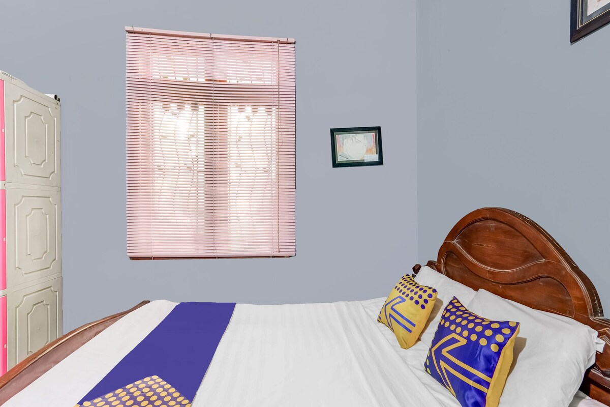 Ein Schlafzimmer mit Bett, einem Fenster mit Jalousien, einem gerahmten Bild an der Wand und einer Tür.