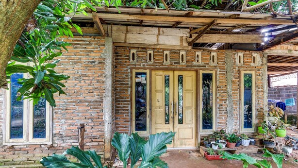 A rustic brick building with a wooden door and windows, surrounded by potted plants. - OYO Homes 91157 Desa Wisata Bendosari Kendal (Bendosari)