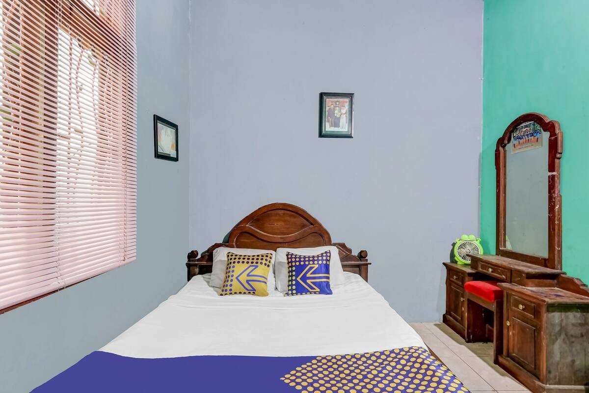 A bedroom with a bed, a dresser, a mirror, and a window with blinds.