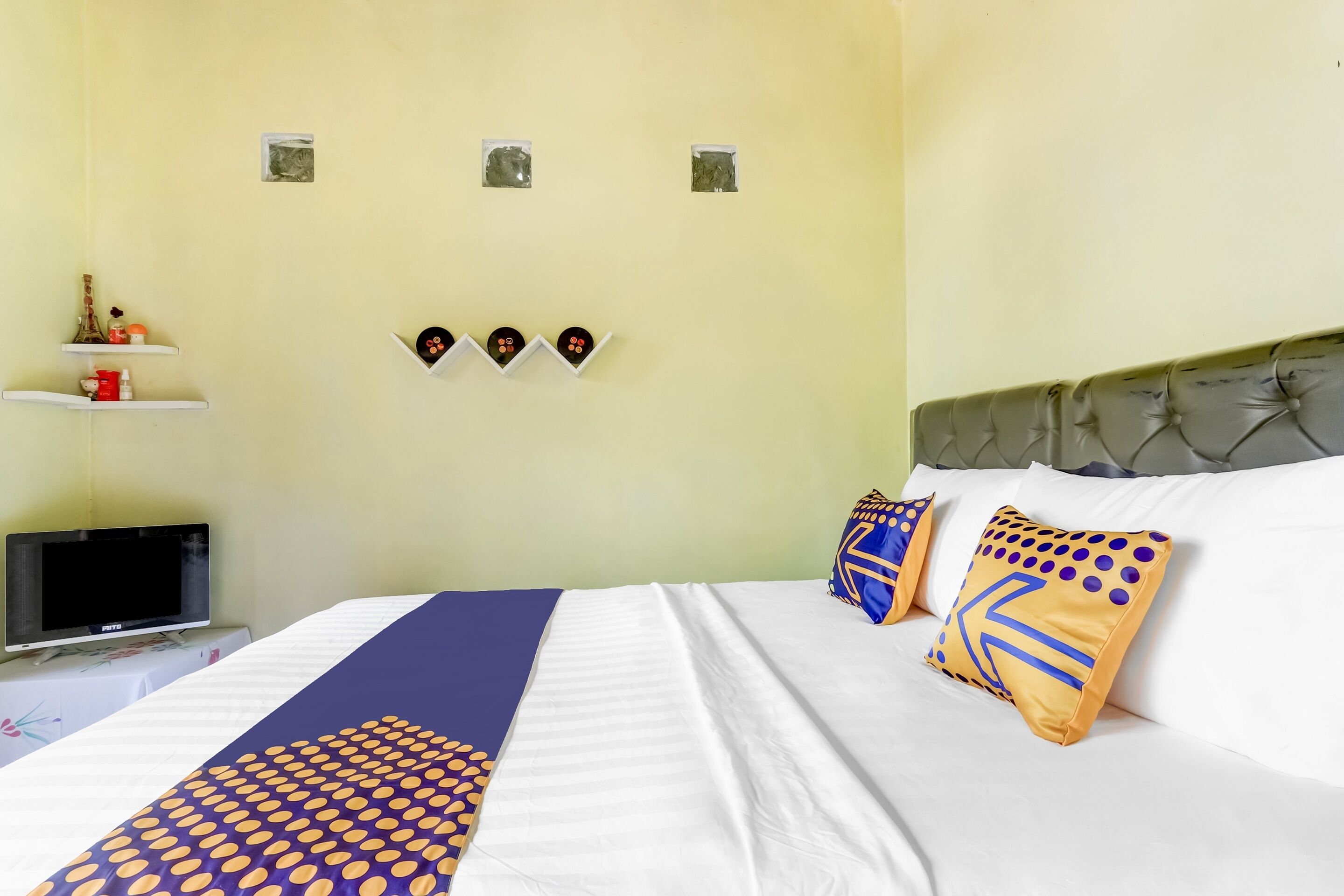 A hotel room with a bed, a television on a stand, and wall decorations.