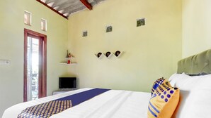 A hotel room with a bed, a television, a window, and a wall-mounted shelf with decorative items. - OYO Homes 91157 Desa Wisata Bendosari Kendal (Bendosari)