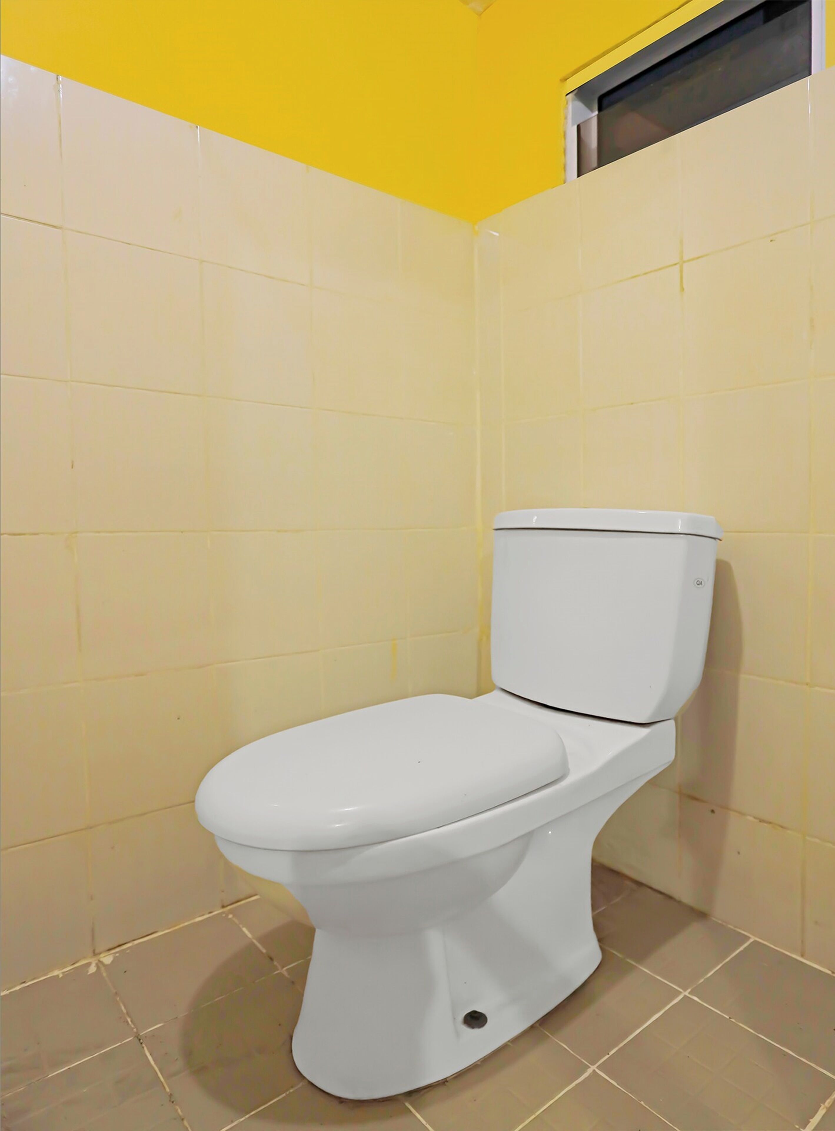 A white toilet in a bathroom with yellow walls and a window above it.