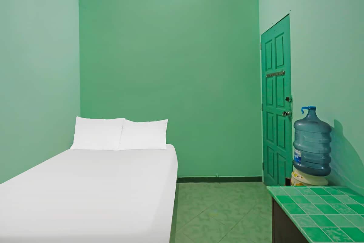 Una habitación pequeña con una cama, dispensador de agua y una puerta verde.