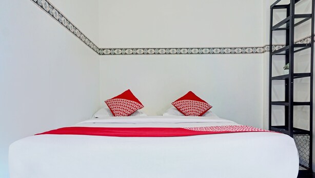 A neatly made bed with white and red bedding, a patterned pillow, and a tiled wall with a decorative border. - Hotel O Bumi Merpati Residence (Makassar)