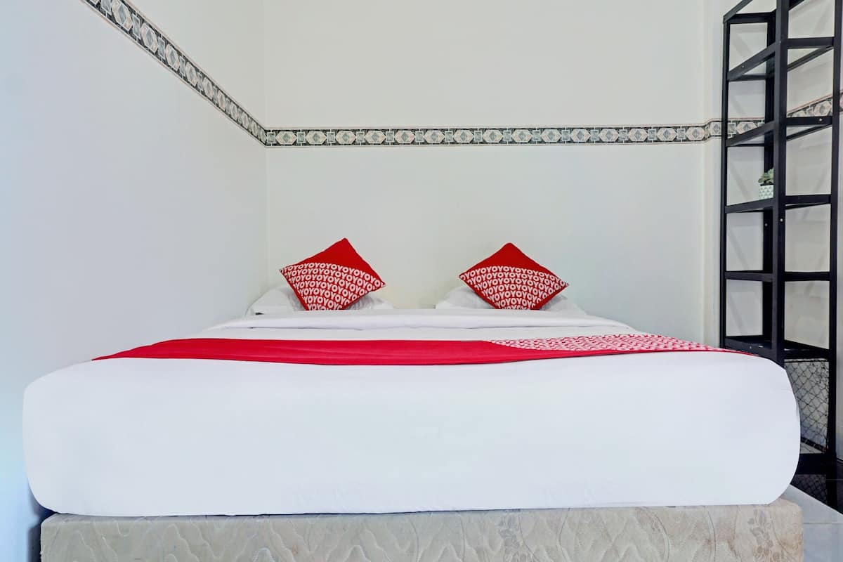 Ein ordentlich bezogenes Bett mit weißer und roter Bettwäsche, einem gemusterten Kissen und einer gefliesten Wand mit dekorativer Bordüre.