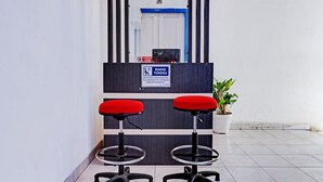 A reception area with two red cushioned chairs, a potted plant, and a sign indicating a health and safety protocol. - Hotel O Bumi Merpati Residence (Makassar)