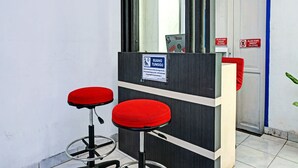A reception area with a counter, two red stools, and a sign indicating a waiting area. - Hotel O Bumi Merpati Residence (Makassar)