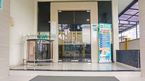 Entrada de hotel com balcão de recepção, elevador de vidro e placa com informações do hotel.