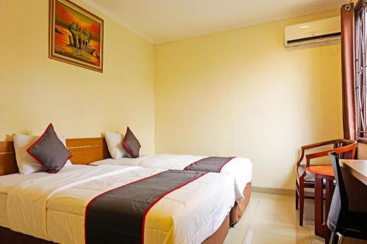 A hotel room with a bed, a desk, and an air conditioning unit.