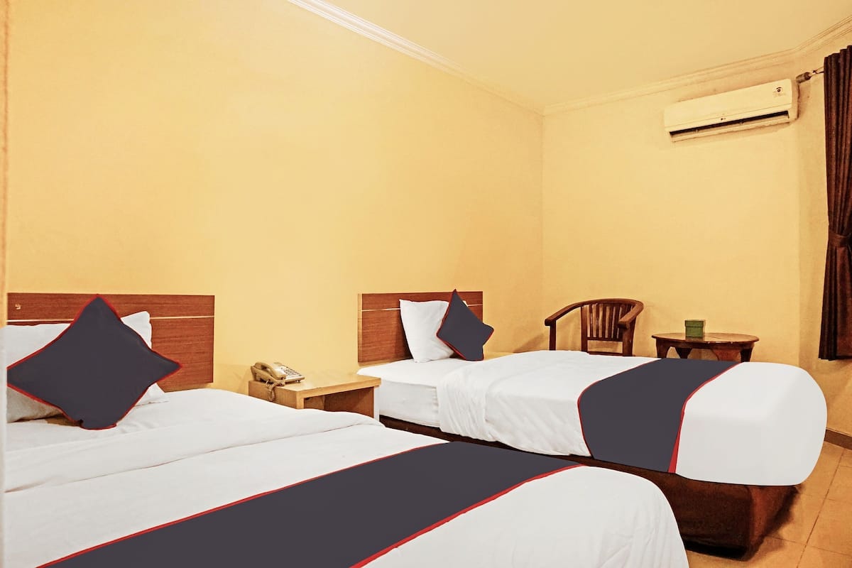 A hotel room with two beds, a wooden headboard, a nightstand, a chair, a small table, and an air conditioning unit.