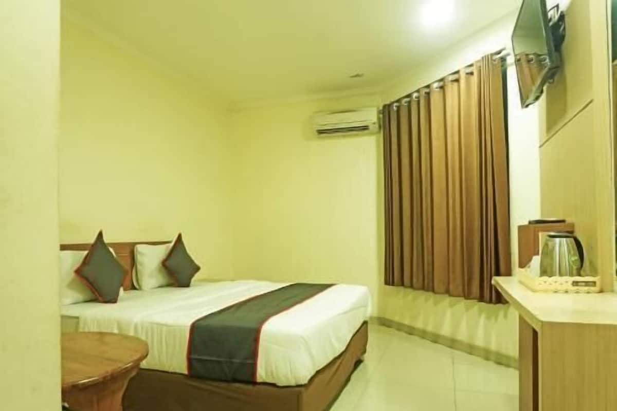 A hotel room with a bed, a small table, a TV mounted on the wall, and an air conditioning unit.