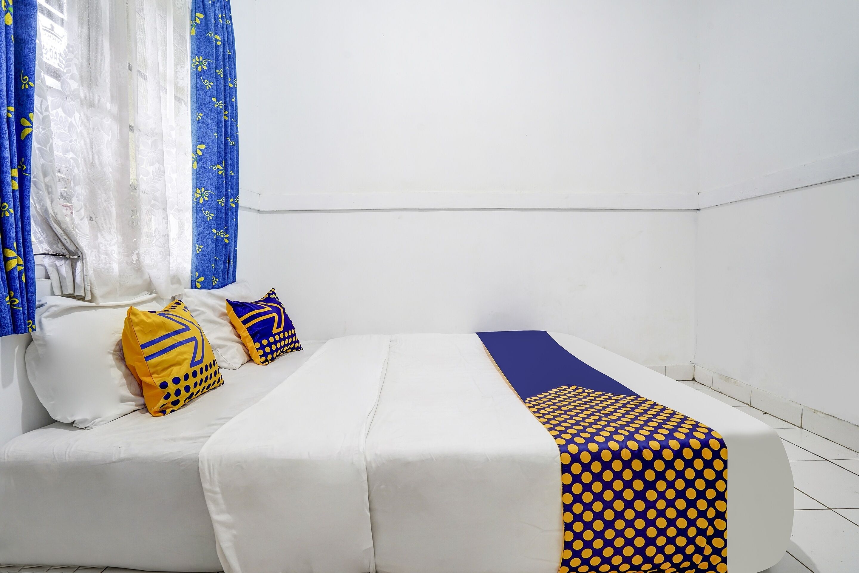 A room with a bed, a blue and yellow patterned blanket, and a white pillow with a yellow design.