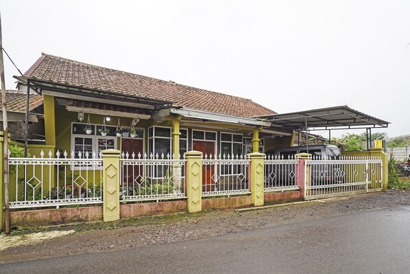 Una casa de dos pisos con techo de tejas, patio cercado y un automóvil estacionado.