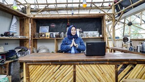 Una cafetería rústica con estructura de bambú, una computadora portátil sobre la barra y diverso equipo para preparar café.